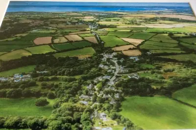 an aerial view of a green field with the ocean at Lovely Cornish cottage in small village setting in Saint Hilary