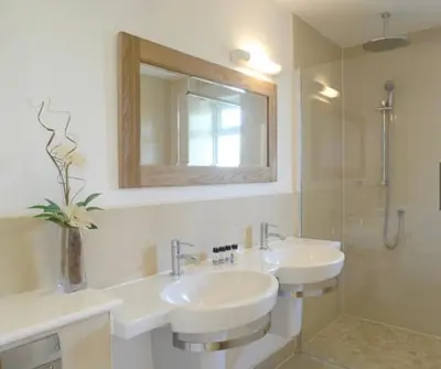 a bathroom with two sinks and a mirror and a shower at Trevone House with Hot Tub on Retallack Resort in Padstow