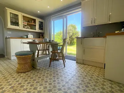 a kitchen with a table and chairs and a window at Baywatch Mawgan Porth Spacious Home sleeps 9, Games room, Parking & Garden in Mawgan Porth