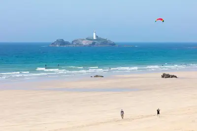two people standing on a beach with a lighthouse in the ocean at Loggans Lodge in Hayle