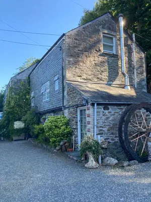 a stone house with a large wheel in front of it at The Granary at Bissick Old Mill in Truro