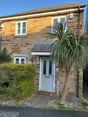 a brick house with a white door and a palm tree at Stylish 3 bed home with allocated parking for 2 in Liskeard