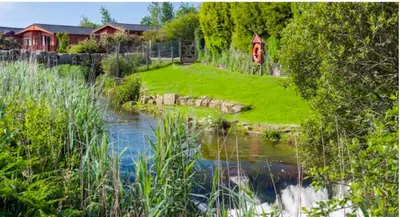 a garden with a river and a house in the background at Gold 10 - Cornish Coastal Retreats in Saint Hilary