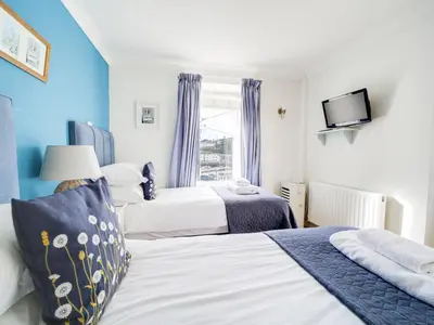two beds in a bedroom with blue walls and a window at The Artist Loft, Ensuite Guest Rooms, Porthleven in Porthleven