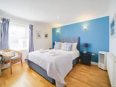 a blue bedroom with a bed and a chair at The Artist Loft, Ensuite Guest Rooms, Porthleven in Porthleven