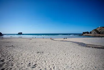 a beach with people walking on the sand and the ocean at Tralee in Portreath