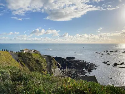 a bench on the side of a cliff overlooking the ocean at Honeysuckle Cottage in Cury