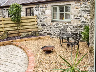 a garden with a table and a chair in front of a building at Honeysuckle Cottage in Cury