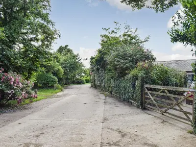 an empty road with a fence and flowers at Honeysuckle Cottage in Cury