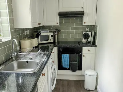 a small kitchen with white cabinets and a sink at The Steps in Pentewan