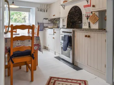 a kitchen with white cabinets and a table and a stove at Zion Cottage in St Austell