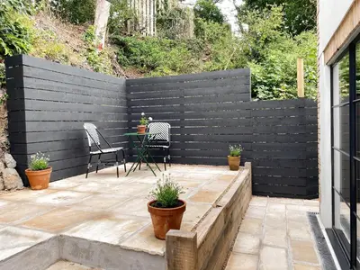 a black privacy fence with a table and chairs on a patio at Luxury bolthole in central St.Agnes with parking. in St. Agnes