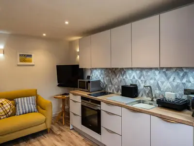 a kitchen with white cabinets and a yellow couch at The Snug in Wadebridge
