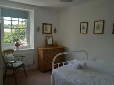 a bedroom with a bed and a chair and a window at The Captain's House Charlestown St Austell in Charlestown