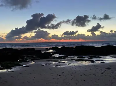 a sunset on a beach with rocks and the ocean at Lovely 2 Bedroom flat moments from Fistral Newquay in Newquay