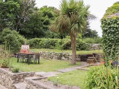 a table and chair in a garden with a palm tree at Myrtle Cottage in Hayle