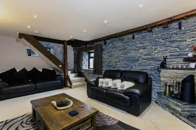 a living room with a leather couch and a stone wall at White Hart Cottage, Menheniot, Nr Looe in Menheniot