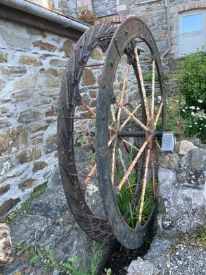 a large wooden wheel leaning against a stone wall at Bissick Old Mill Suite in Truro