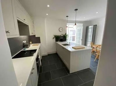 a kitchen with white cabinets and a black tile floor at Beautiful 2 bed end terrace Victorian town house in Redruth