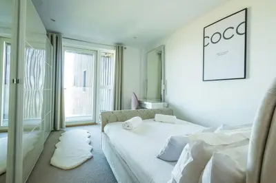 a white bedroom with a bed and a mirror at Luxury beach apartment in Perranporth