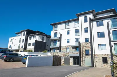 a large white building with cars parked in a parking lot at Luxury beach apartment in Perranporth