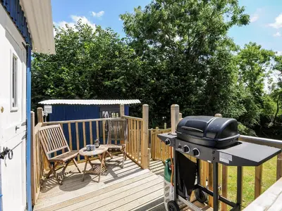 a grill on a deck with a table and chairs at Shepherds Hut in Lostwithiel