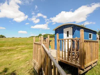 a blue shack in a field with a wooden fence at Shepherds Hut in Lostwithiel
