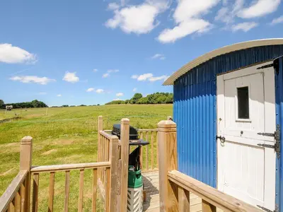 a blue shed with a fence and a field at Shepherds Hut in Lostwithiel