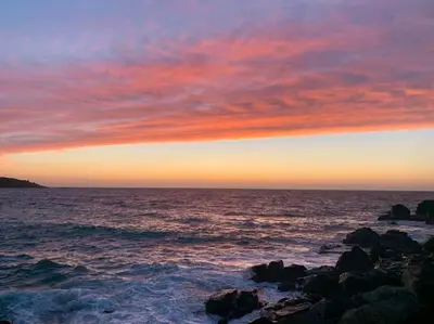 a sunset over the ocean with rocks in the water at High quality detached house with parking St. Ives in St Ives