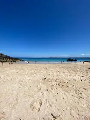 a sandy beach with people in the water and the ocean at Sandals cottage in St Ives