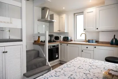 a small kitchen with white cabinets and a staircase at Sandals cottage in St Ives