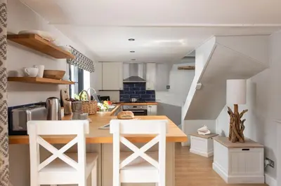 a kitchen with a table and two white stools at Spindrift, St Ives in St Ives