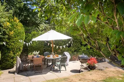 a patio with a table with an umbrella and a grill at Pump Cottage in Gwithian