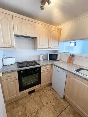 a kitchen with wooden cabinets and a stove and a sink at 1 Chatsworth Riverscape Apartments - Riverview apartment in great location with free parking overlooking the Gannel just a short walk from Newquays incredible beaches and local amenities in Newquay