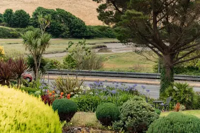 a garden with flowers and a train on a road at 1 Chatsworth Riverscape Apartments - Riverview apartment in great location with free parking overlooking the Gannel just a short walk from Newquays incredible beaches and local amenities in Newquay