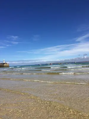 a beach with the ocean and a lighthouse in the background at Tranquil Retreat at River Valley Country Park in Penzance