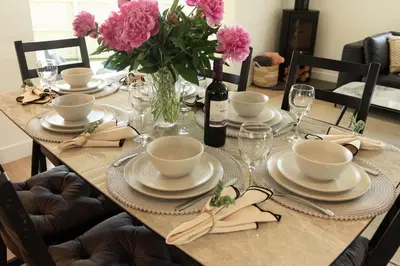 a dining room table with pink flowers and a bottle of wine at Sandy Cove in Penzance