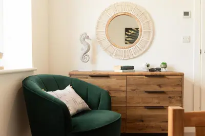 a green chair next to a dresser with a mirror at Sandy Cove in Penzance