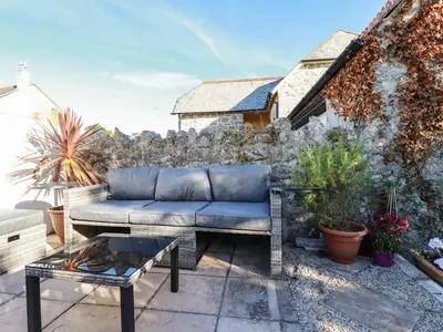 a couch on a patio with a stone wall at Carminow Barn in Bodmin