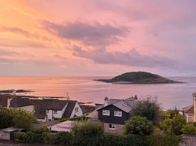 a sunset over a town with a small island in the water at Sea Spirit - Sweeping Sea Views first floor spacious modern apartment in Looe- with FREE parking! in Looe