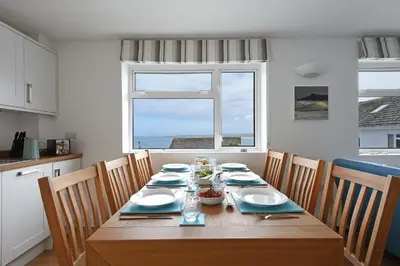 a dining room table with chairs and a large window at St Ives Bay View in Carbis Bay