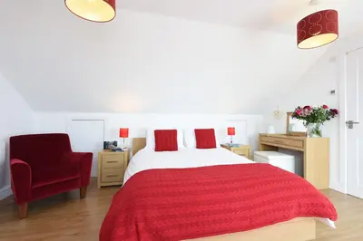 a bedroom with a bed with a red blanket and a chair at St Ives Bay View in Carbis Bay