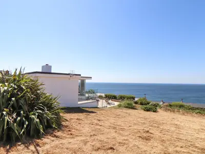 a house on the beach with the ocean in the background at Boscregan in Helston