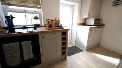 a kitchen with white cabinets and a counter with a window at Padstow Escapes - Captains Cottage in Padstow