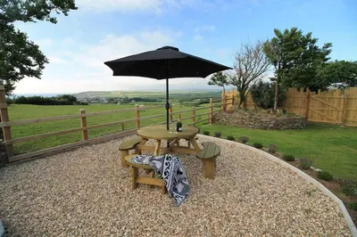 a picnic table with an umbrella and a bench at Sea View at Widemouth Bay - 3 bedroom cottage in Poundstock