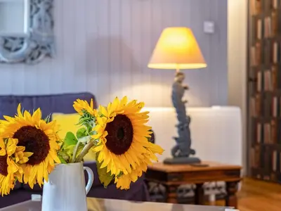 a vase of sunflowers on a table with a lamp at Pibbies in Port Isaac