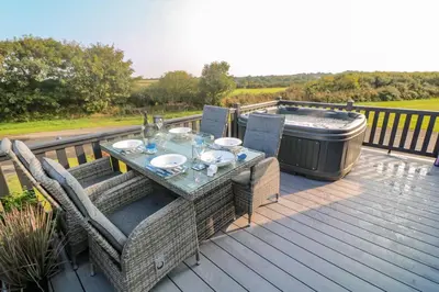 a table and chairs on a deck with a hot tub at Chantry Lodge in Newquay
