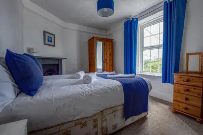 a bedroom with a bed with blue curtains and a window at Coastguard Cottage Cornwall - Sea & Harbour Views in Mevagissey