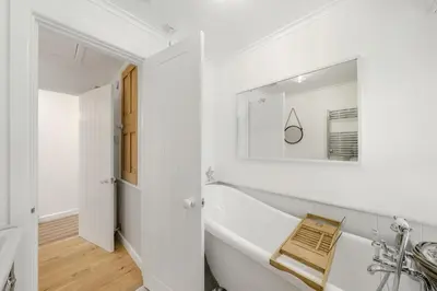 a white bathroom with a tub and a mirror at Jade Cottage in St. Agnes