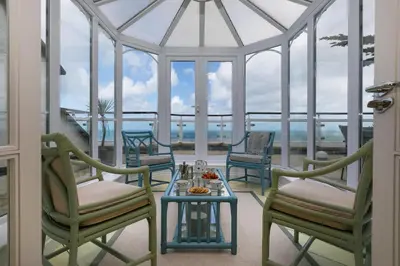 a conservatory with chairs and a table on a balcony at Ocean Gem in Carbis Bay